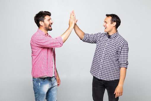 Full length portrait of two happy young men giving high five isolated over white background