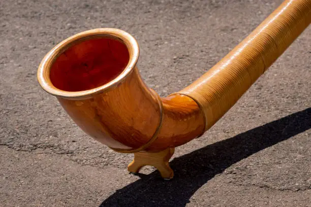 A close up view of the end of wooden Alphorn (Alpenhorn or Alpine horn) on a concrete background. Traditional instrument in Switzerland