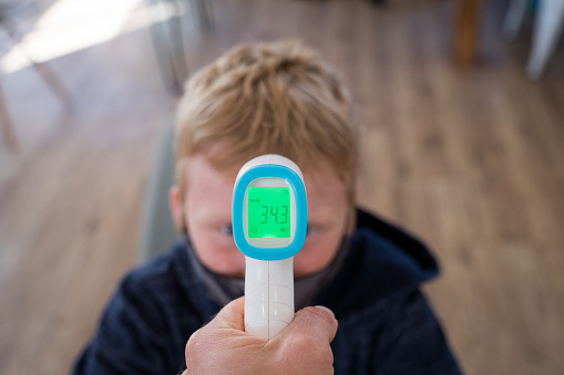 POV of a schoolboy having his temperature taken before school. Teacher uses a infrared thermometer to test students for signs of COVID-19.