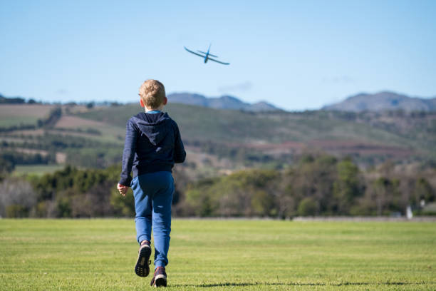 Cute child of Indian ethnicity sitting outdoor in the nature & playing with airplane toy alone.