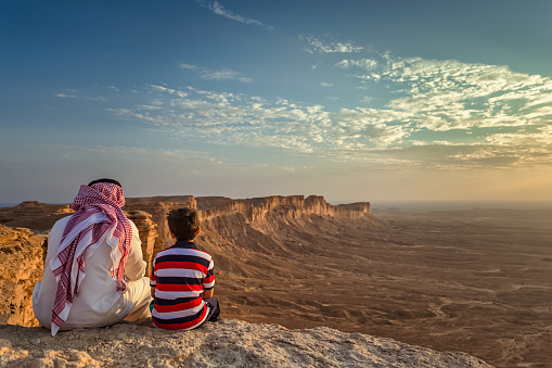 An arab man and his son sitting in Edge of the world, a natural landmark and popular tourist destination near Riyadh -Saudi Arabia.08-Nov-2019. Selective focus and background blurred.