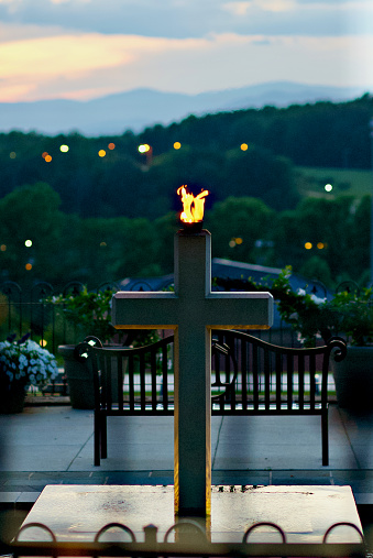 Lynchburg, Virginia / USA - June 29, 2020: A flame burns brightly from a cross-shaped memorial adjacent to the grave of Rev. Jerry Falwell, Sr., on the grounds of historic Montview Mansion, itself on the campus of Liberty University that Falwell founded in 1971.