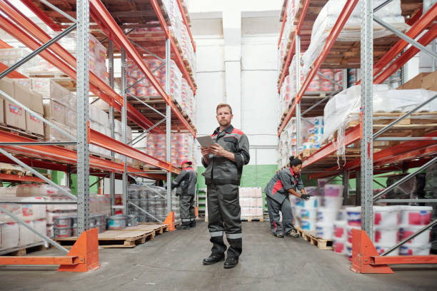istock Serious young male worker of warehouse in uniform using tablet between racks 1264679504