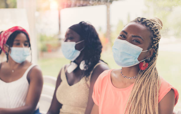 Close-up of three African American girls wearing surgical masks. Close-up of three African American girls wearing surgical masks. 3 young women sitting together using coronavirus protection measures after or during quarantine. Concept of new normal lifestyle. new normal concept stock pictures, royalty-free photos & images