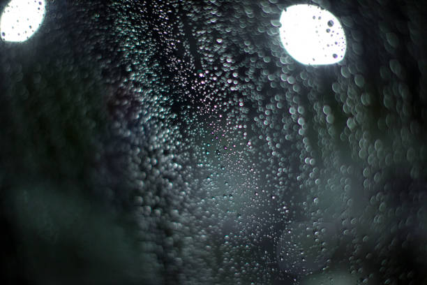 Close-up photo of a lot of raindrops on a car window shining on a streetlight at night.