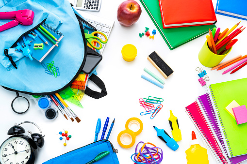 Back to school concepts: high angle view of multi colored school supplies isolated on white background. A computer keyboard, a smart phone and a black alarm clock are included in the composition. High resolution 42Mp studio digital capture taken with SONY A7rII and Zeiss Batis 40mm F2.0 CF lens