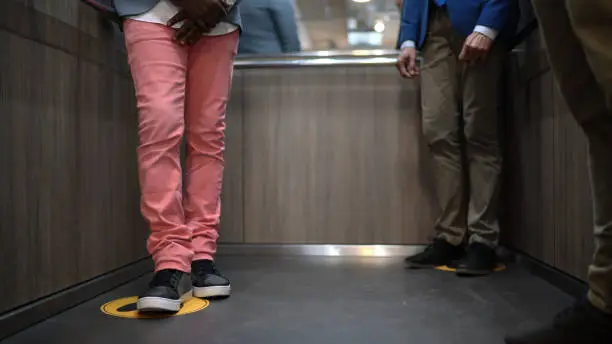 Photo of Low sectiong of men standing in marked areas, for social distancing, in the lift