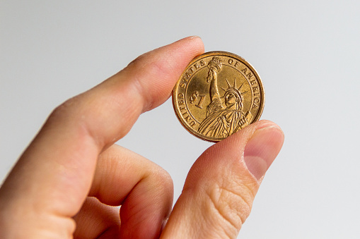 United States one dollar coin with Liberty Statue being held by fingers.