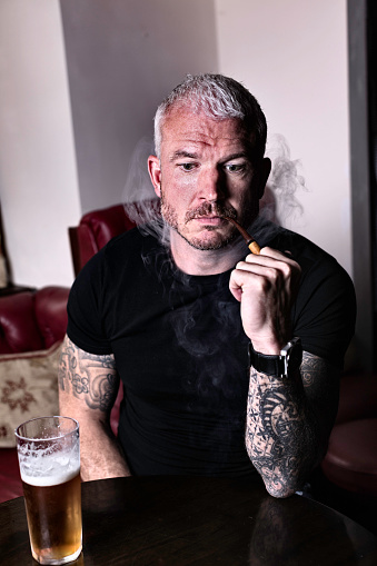 Portrait of a workman in his 40s enjoying a pint of beer and a smoke of his pipe.