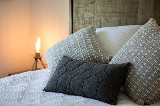 Closeup of new bed comforter with decorative pillows, headboard in bedroom in staging model home, house or apartment