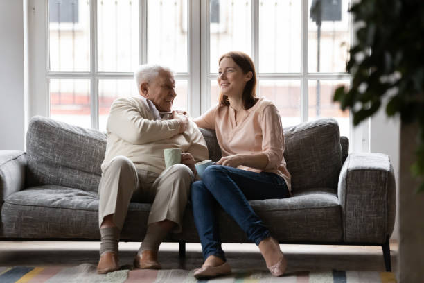 Happy older man and adult daughter drinking tea together Happy older man and adult daughter drinking tea or coffee together, sitting on cozy couch, smiling young woman and mature father having fun, enjoying leisure time, talking, sharing news father daughter 80s stock pictures, royalty-free photos & images