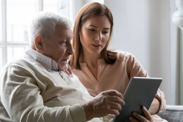 Caring grownup daughter teaching elderly father to use tablet Caring grownup daughter teaching older father to use computer tablet close up, pointing at screen, mature man asking questions about mobile device to young woman, elderly and technology concept father daughter 80s stock pictures, royalty-free photos & images