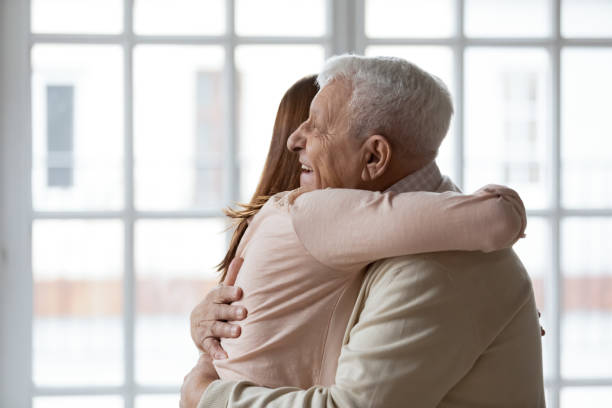 Close up happy older mature man hugging grownup daughter Close up happy older mature man hugging grownup daughter or granddaughter, standing at home together, family enjoying tender moment, two generations, young woman embracing elderly father father daughter 80s stock pictures, royalty-free photos & images