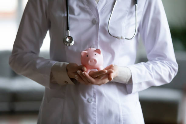 Close up young female doctor holding pink piggy bank Close up young female doctor therapist wearing white coat uniform and stethoscope holding pink piggy bank, healthcare money savings, medical insurance concept, hospital budget and accounting operating budget stock pictures, royalty-free photos & images