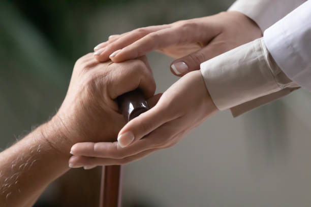 istock Close up female caregiver touching elderly disabled patient hand 1264699622