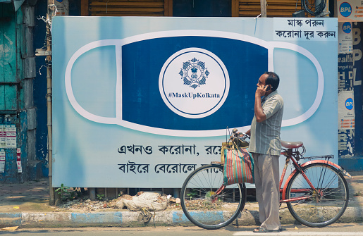 Kolkata, 07/26/2020: A middle aged person standing with his cycle in front of a Kolkata Police awareness banner urging people to wear face mask. He is returning from bazaar.