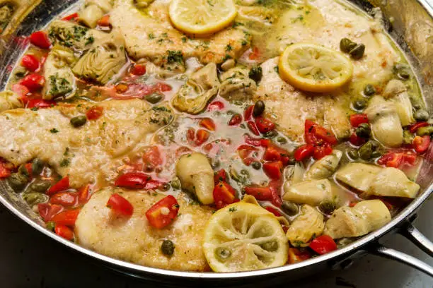 Italian chicken piccata with artichoke hearts and capers cooking in large pan