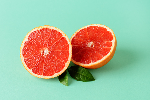 Two halves of fresh ripe juicy grapefruit and two leaves on a mint green background. Vegetarian, raw food diet and healthy eating. Organic antioxidant. Front view.