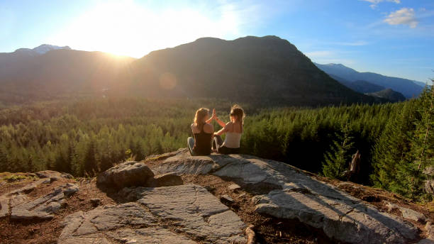 young women relax on rock slabs, look off to view - growth tree spirituality tranquil scene imagens e fotografias de stock