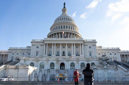 Couple take photos in-front steps to the US Capitol Building, west side on sunny day.