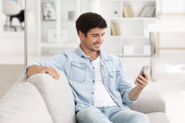 istock Young happy man sitting relaxed on sofa and talking on the phone, mobile video call. 1264718530