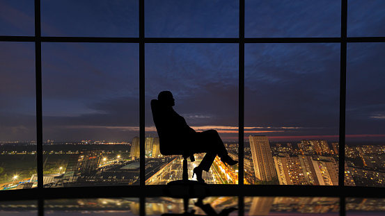 The business woman sits in the office near the windows with a night city view