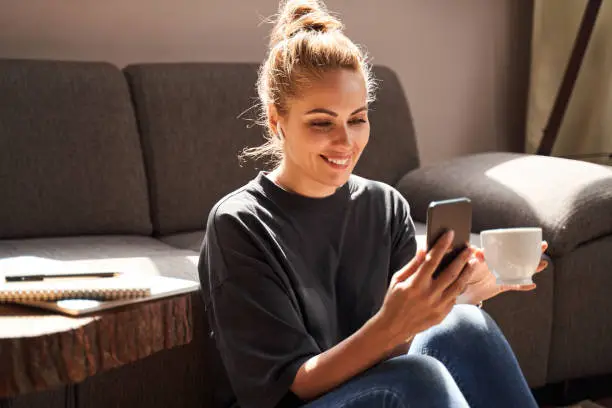 Photo of Contented lady smiling while using her smartphone at home