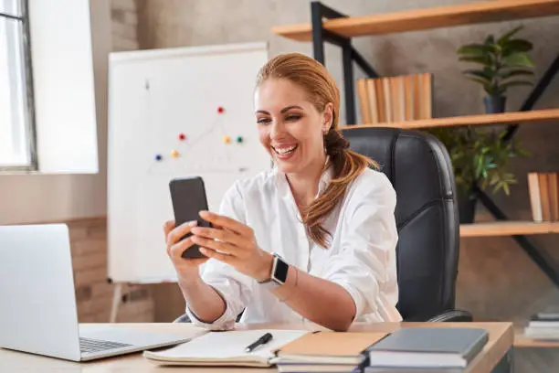 Photo of Mirthful lady having video call at work and smiling