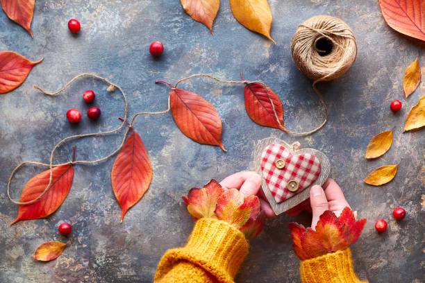 istock Autumn decorations made from natural materials, bright Fall leaves. Hands in orange sweater hold wooden heart. Seasonal Fall flat lay. 1264721450