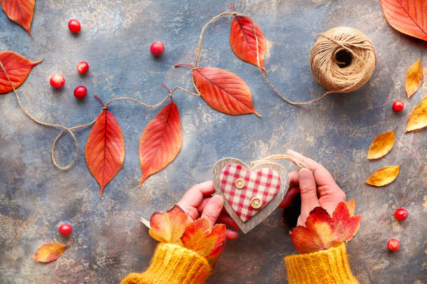 istock Autumn decorations from natural materials, vibrant Fall leaves. Hands in orange sweater hold wooden heart. Seasonal Fall flat lay. 1264721517