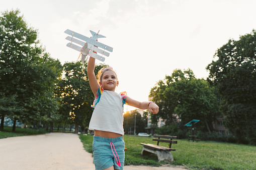 Photo of a cheerful little girl, running down the field with her airplane toy