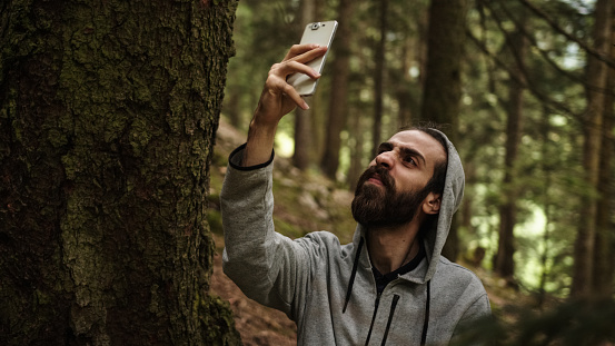 Hipster teenager texting in the forest with a phone in his hand breaks the signal, stressed young man with signal problems