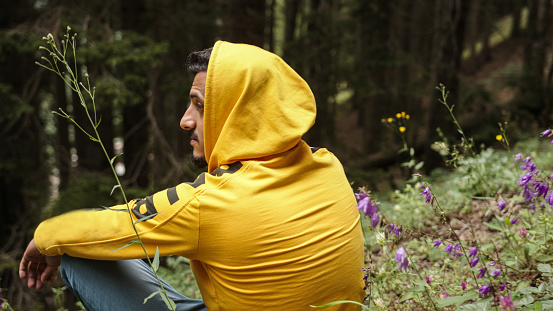 Hoodie man is sitting in the trees in the forest, looking left and right and relaxing