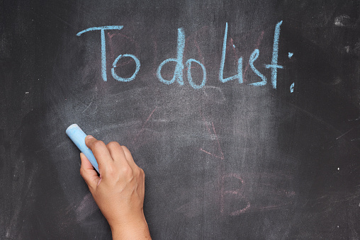 inscription to do list on a black chalk board and a female hand with blue chalk, the concept of future planning, strategy