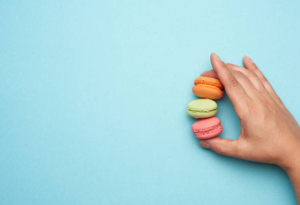 istock female hand holds three round baked macarons cookies on a blue background 1264729779