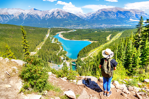 Hiker standing on top of Grassi Lakes trail overlooking the town of Canmore in Kananaskis with scenic Rundle Forebay Lake and Canadian Rockies in the background.