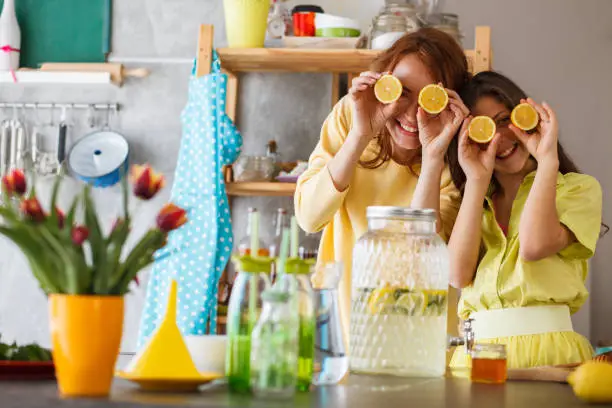 Front view of happy female family members playing with lemons as eyes after making tasty refreshing lemon juice in a colorful kitchen.