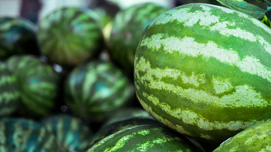 In natural and organic farmer's market, striped water melon fruits are stacked in a surface as background.