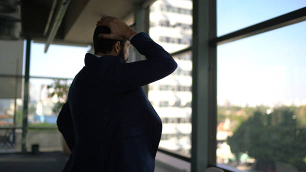 istock Worried businessman looking through window contemplating on the office 1264741464