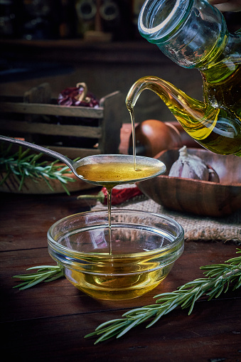 Female hand pouring olive oil from bottle to container with olives. Arrange on table in old fashioned rustic kitchen.