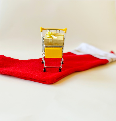 Miniature yellow shopping cart with beautifully wrapped presents on bright red holiday stocking