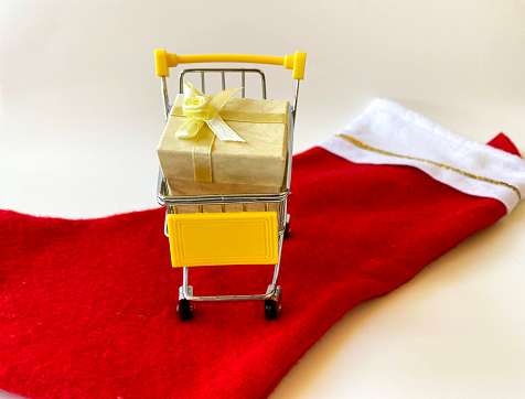 Miniature yellow shopping cart with beautifully wrapped presents on bright red holiday stocking