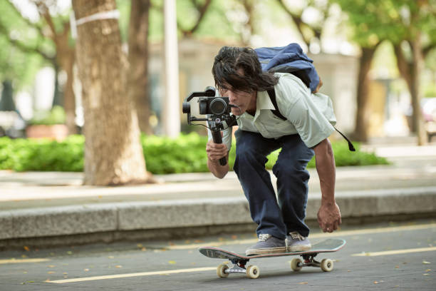 Asian skateboarder filming using video recorder with gimbal Asian young man with skateboard shooting video with gimbal extreme skateboarding stock pictures, royalty-free photos & images