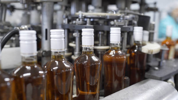 istock Glass bottles filled with prune tincture move along conveyor line with control panel in modern distillery for bottling alcoholic beverages. Production process of alcoholic beverages in factory. 1264770407