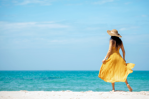 Summer vacations. Lifestyle woman relax and chill on beach background.  Asia happy young people wearing yellow dress fashion summer trips walking enjoy  tropical beach. Lifestyle and Travel Concept.