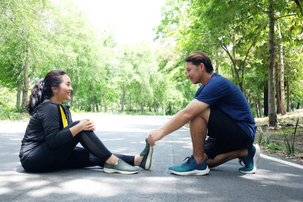 아시아의 젊은 여성 스포츠웨어는 그녀의 다리와 남자 친구를 경련시키고, 정원�에서 실행하고 실행 후 탄력과 근육 수축의 휴식을 돕고있다. - cramping 뉴스 사진 이미지