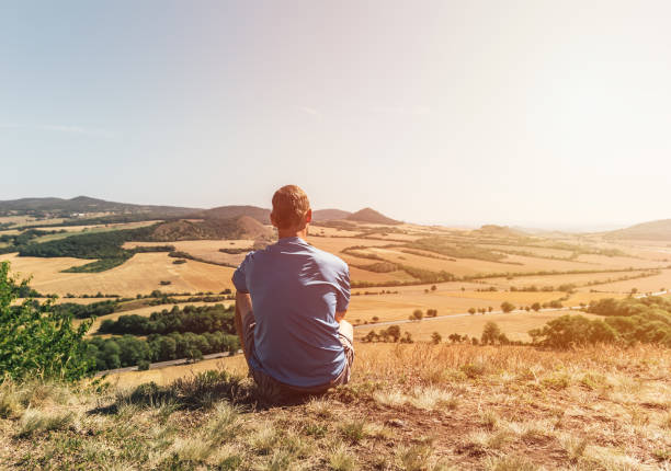 istock Young man sitting on hill and looking to Czech central mountain valley 1264788709