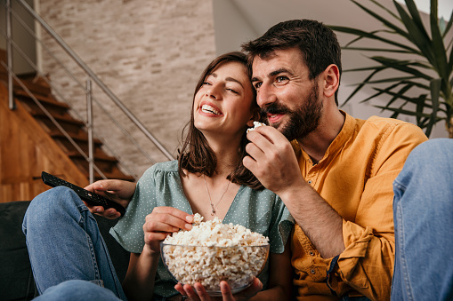 Young adorable happy couple sitting at home, hugging and watching a television. Relaxation after work.