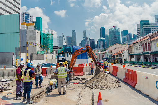 Singapore, Oct 2019: Workers in uniforms repairing road surface in city downtown. Modern skyscrapers in the background. Road blocked due to roadworks