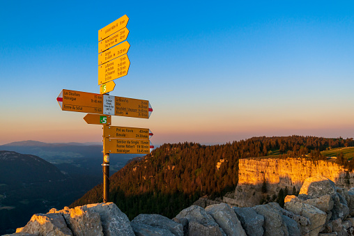at the Creux du Van canyon with colorful skies shortly after sunset in the swiss jura mountains. Signpost at an old stone wall that leads along the hiking trail. 05/29/2020 canton of neuchâtel, Switzerland